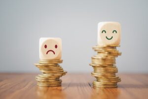 Two stacks of coins with blocks on top, one sad face on a shorter stack and a happy face on a taller stack.