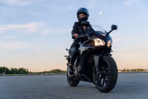 A motorcyclist wearing a helmet and leather gear sits on a black motorcycle, ready to ride.