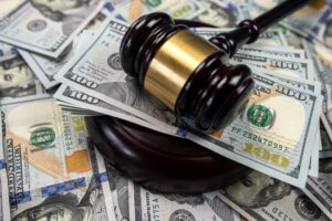 Judge's gavel resting on a pile of hundred-dollar bills, symbolizing financial settlements in legal cases.