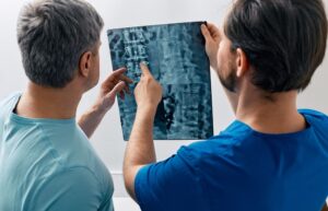 Two doctors examine a spinal X-ray, discussing the condition of the patient's spine.