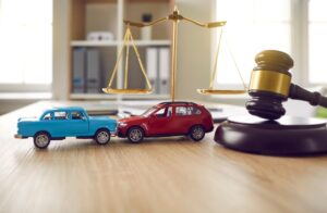 Toy cars in a collision beside scales of justice and a gavel, symbolizing legal action.