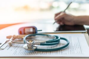 Stethoscope on medical forms, with a person writing, symbolizing a fresh start after a health exam.