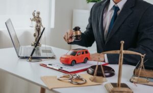 Lawyer at a desk with a gavel, toy car, scales of justice, and laptop.