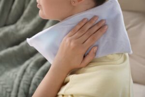 Close-up of a woman applying a cold compress to her neck, soothing a soft tissue injury.