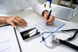 Person calculating medical expenses with a stethoscope, calendar, and laptop on the desk.