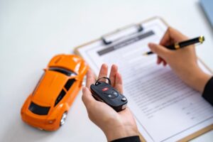 Person signing a contract while holding car keys, with a toy car on the desk.