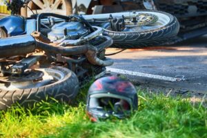 A crashed motorcycle lying on the ground beside a road, with a helmet nearby.