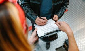 A person signs documents on a clipboard, possibly related to a motorcycle accident claim.