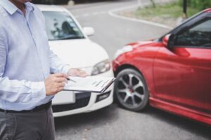 An insurance agent filling out a report form for a traffic accident claim, with a notepad and pen in hand, illustrating the car accident insurance process.