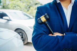 Lawyer holding a wooden gavel stands in front of a car, discussing legal aspects such as citations, liability, and negligence related to a traffic violation