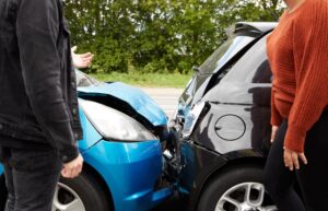 Two angry motorists standing beside their damaged cars, arguing over who is responsible for a car accident.