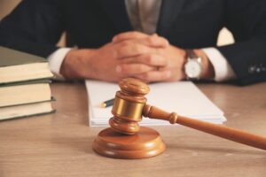 Man's hand holding a wooden gavel next to a legal document, symbolizing justice and courtroom proceedings.